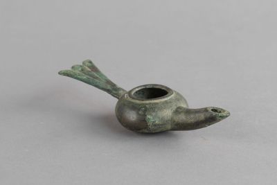 une vieille pipe en bronze en forme d'oiseau posée sur une surface grise