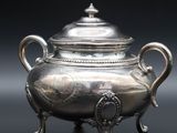 une théière ancienne en argent posée sur un support, sur fond noir