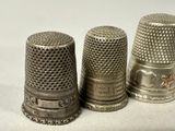 three silver thimbles are lined up on a white surface