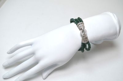 une main de mannequin blanche à laquelle est attaché un bracelet vert