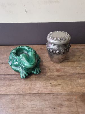 a green frog sitting next to a silver container on a wooden table