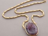 a close up of a necklace with a purple stone on a gold chain