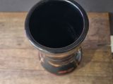 a black cup sitting on a wooden table next to a white wall