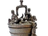 un petit récipient en métal surmonté d'une statuette