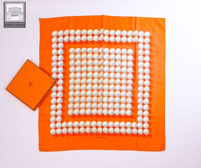 une écharpe carrée orange et blanche, ornée de boules blanches