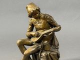 bronze statue of a man sitting on a rock playing a guitar
