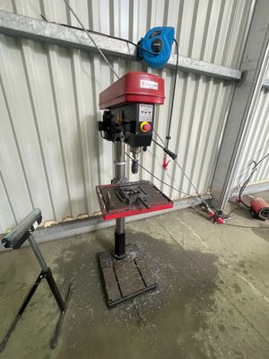 une perceuse à colonne dans un garage, avec un souffleur bleu