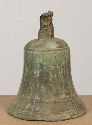 une vieille cloche posée sur une table en bois près d'un mur blanc
