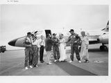 photographie en noir et blanc d'un groupe de personnes debout devant un avion