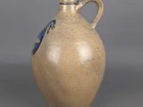 a brown vase with a blue handle on a gray surface
