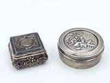 une petite boîte en argent et une petite boîte en argent posées sur une surface blanche