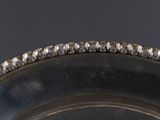 an antique silver plate with a beaded edge on a black background
