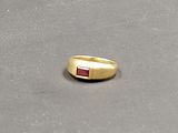 une bague en or sertie d'une pierre rouge, posée sur une table