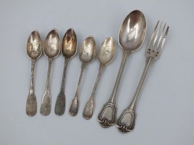 six silver spoons and a fork are lined up on a white surface