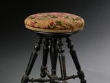 un tabouret ancien avec une assise rembourrée à motifs floraux et des pieds en bois