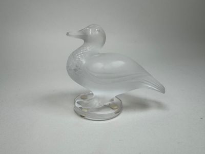 un canard en verre posé sur un socle transparent