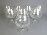 six verres à vin vides sont alignés sur une surface grise