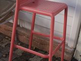 an image of a red plastic bar stool on a brick patio