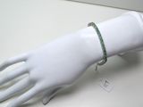 une main de mannequin blanche à laquelle est enfilé un bracelet vert