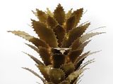 a close up of a metal pineapple plant on a white surface