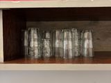 bottles and glasses are lined up on a shelf against a red wall