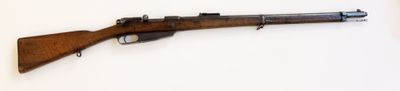 fusil posé sur une surface blanche, muni d'une crosse en bois et d'une poignée en métal
