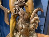 bronze statue of a man with a knife and a rooster on a table