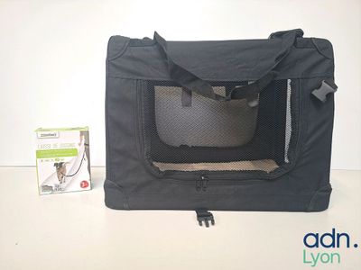 un petit chien noir dans une cage de transport, à côté d'un carton