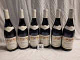 six bottles of red wine are lined up on a table