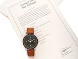 une montre posée sur une feuille de papier, à côté d'une autre feuille de papier