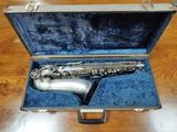 un saxophone argenté dans un étui bleu, posé sur un plancher en bois