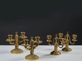 trois chandeliers en laiton posés sur une table blanche, sur fond noir