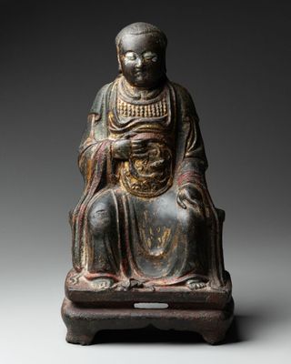 une vieille statue représentant un homme assis sur un tabouret