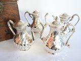 trois théières en argent posées sur une table à côté d'une boîte en bois