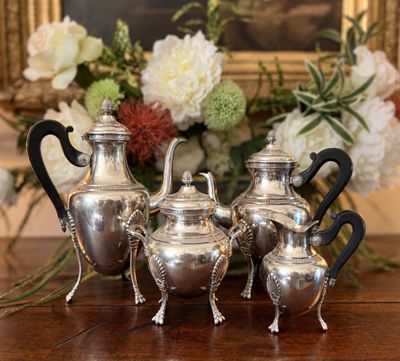 quatre théières en argent posées sur une table, avec des fleurs en arrière-plan