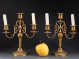 three brass candelabs with white candles and an apple on a table