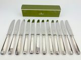 six silverplated knives and a box of knives on a white surface