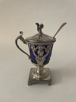 une tasse en argent surmontée d'une cuillère, posée sur une surface blanche