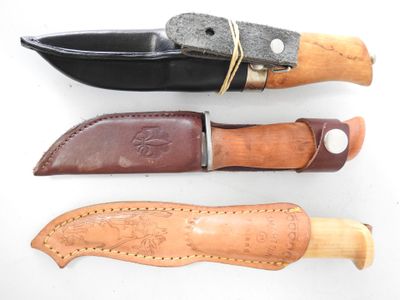 three different types of knifes with leather sheaths on a white surface
