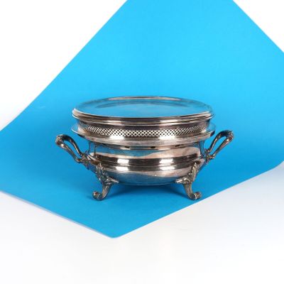un plat en argent muni d'un couvercle, posé sur un fond bleu