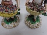 two figurines of a man and a woman holding baskets of flowers