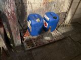 two blue barrels sitting next to each other on the sidewalk
