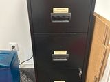 a black filing cabinet next to a blue trash can
