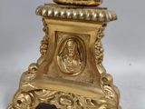 a gold clock on a stand with a bird on it