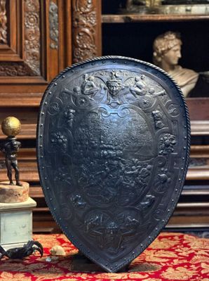 un grand bouclier métallique posé sur une table à côté d'une statue