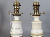 une paire de lampes blanches et dorées posées sur une étagère, avec un tableau accroché au mur en arrière-plan