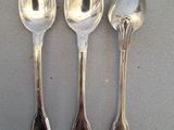 three silver spoons are lined up on a gray surface