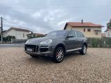 a grey porsche cayen is parked in a gravel lot
