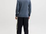 a man standing in front of a white background wearing a blue sweater and black pants