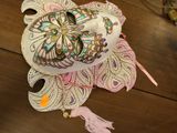 un masque blanc posé sur une table en bois, orné d'un pompon rose